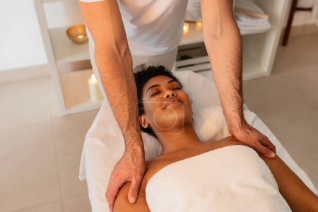 Téléchargez les photos : Une image tranquille représentant un massage des épaules apaisant pour femme afro-américaine par un professionnel dans un environnement spa serein avec un accent sur la médecine alternative - en image libre de droit