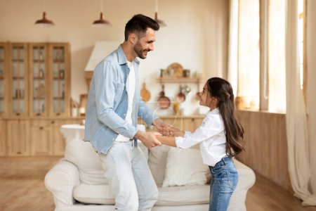 Photo for A delightful moment of a blurry-faced young girl dancing with her father in a bright living room at home - Royalty Free Image