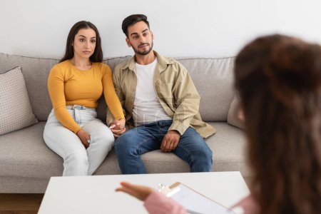Therapeutin mit Klemmbrett im Gespräch mit einem jungen Ehepaar, das in einer Therapiesitzung auf einer Couch sitzt
