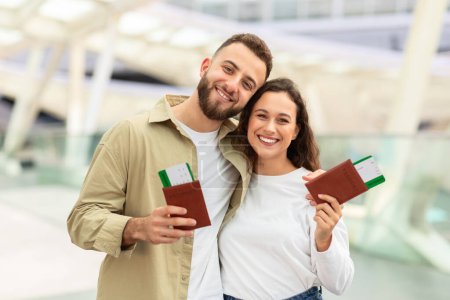 Ein fröhlicher Mann und eine fröhliche Frau halten ihre Reisedokumente in einem hellen Flughafenterminal, bereit für ihren Flug, ein glückliches Paar genießt das gemeinsame Reisen, Kopierraum