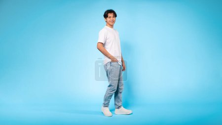 Photo for A side view of a young asian guy in casual attire, standing confidently with a plain blue background - Royalty Free Image