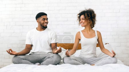 Young african-american family meditating in bed, smiling to each other, copy space