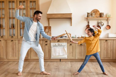 Foto de Padre e hija fingen tener una pelea de espadas con cucharas de madera en un hogar acogedor - Imagen libre de derechos