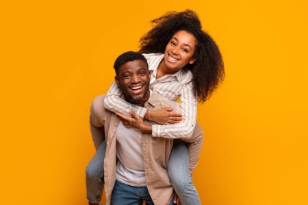 Cheerful African American couple in a playful embrace laughing together on a yellow studio background