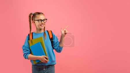 Foto de Colegiala feliz con gafas, trenzas y mochila apuntando al espacio de copia en blanco sobre un fondo rosa - Imagen libre de derechos
