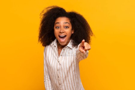 Téléchargez les photos : Heureuse jeune femme afro-américaine avec les cheveux bouclés pointant vers la caméra, fond de couleur vive - en image libre de droit