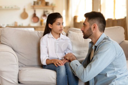 A thoughtful father and his daughter engage in a serious conversation while sitting on a couch at home