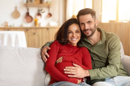 Photo for A joyful young pregnant couple cuddling on a cozy couch in a well-lit living room, with a warm and inviting atmosphere - Royalty Free Image