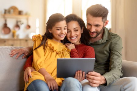 Eine entzückte dreiköpfige Familie sitzt mit einem digitalen Tablet auf der Couch und taucht gemeinsam in die Technik ein