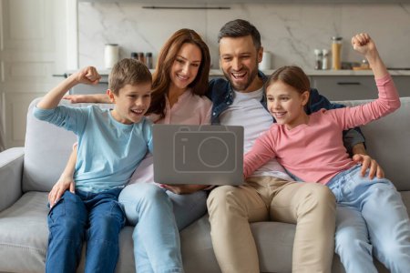 Happy family with two children sitting on a couch and celebrating as they look at a laptop screen at home
