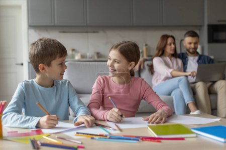 Téléchargez les photos : Deux enfants font leurs devoirs ensemble pendant que les parents utilisent un ordinateur portable en arrière-plan à l'intérieur de la maison - en image libre de droit