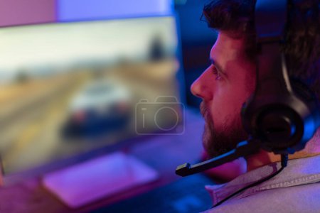 A focused guy gamer with headphones is playing a racing game, showcasing the immersive experience of modern gaming