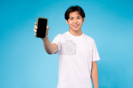 Young Asian guy presenting a smartphone with a blank screen, ideal for mockups or app presentations, cool offer