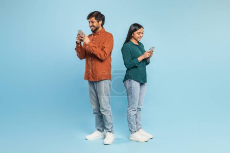 Photo for Engrossed Indian couple standing back-to-back using their smartphones, symbolizing modern communication - Royalty Free Image