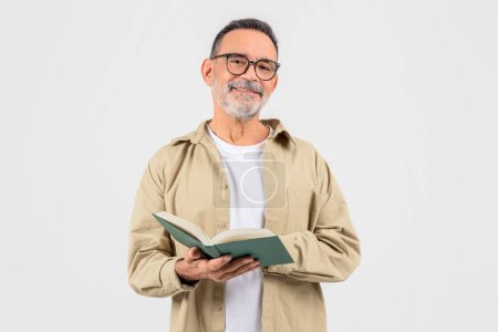Konzentrierter älterer Mann, der sich mit konzentriertem Interesse in ein grünes Buch vertieft und Lern- oder Freizeitlektüre vorschlägt