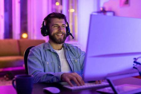 Téléchargez les photos : Homme barbu souriant portant un casque avec microphone aime jouer dans une pièce colorée avec éclairage au néon - en image libre de droit
