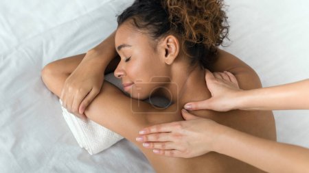 Foto de Mujer afroamericana disfrutando del masaje en los hombros, acostada con los ojos cerrados en el centro de spa - Imagen libre de derechos