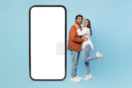 Happy Indian couple standing with a large blank smartphone screen, ideal for app or advertisement mockups