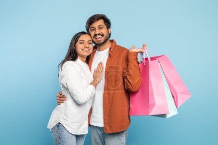 Téléchargez les photos : Couple indien affectueux tenant des sacs à provisions et embrassant chaleureusement, exprimant la proximité après les achats - en image libre de droit