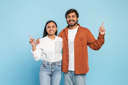 Cheerful Indian man and woman pointing up, suggesting a shared goal or direction, on a blue background