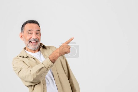 Hombre mayor alegre en atuendo casual apuntando a la derecha con una gran sonrisa en su cara, sugiriendo producto o espacio