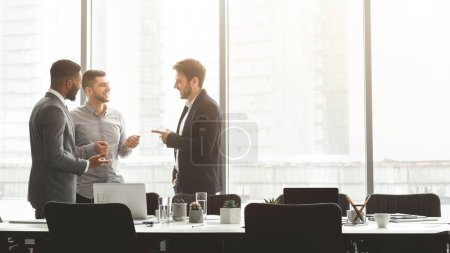 Tres profesionales de la empresa participan en un debate en un entorno de oficina contemporáneo bien iluminado, ejemplificando el trabajo en equipo y la colaboración