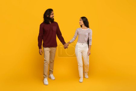 Photo for Two people, a man and a woman, walking and holding hands with a yellow background symbolizing movement - Royalty Free Image