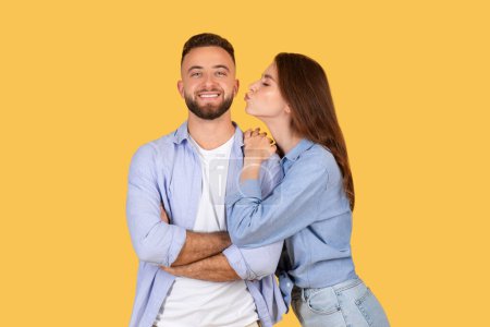 Téléchargez les photos : Une femme embrassant un homme souriant sur la joue sur un fond jaune, à la fois vêtue de façon décontractée et regardant contenu - en image libre de droit