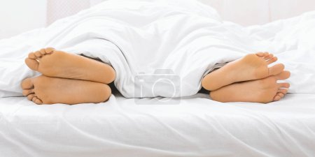 Relaxed and subtle image of a couples feet peeking out from a soft white duvet, representing closeness and comfort