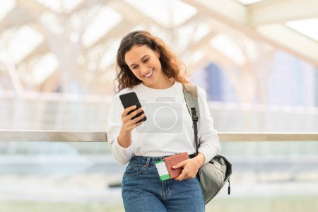 A cheerful woman focused on her mobile phone in a bustling travel environment with travelers nearby