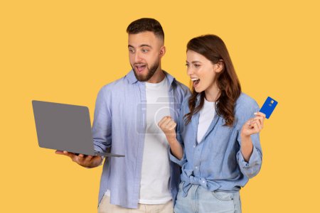 Man and woman excitedly look at a laptop screen with a credit card, implying an online purchase