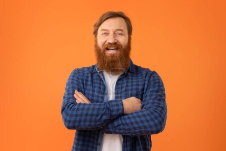 Photo for Successful Person. Portrait of funny European redhaired man with beard in glasses standing with crossed hands over orange studio wall, smiling and laughing expressing positivity - Royalty Free Image
