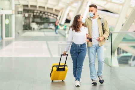 Foto de Una joven pareja con máscara facial, camina con equipaje en un aeropuerto moderno - Imagen libre de derechos