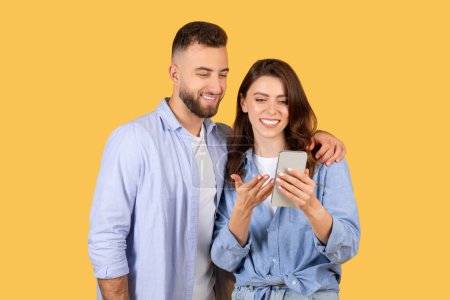 Happy man and woman looking at a mobile phone together with a yellow background