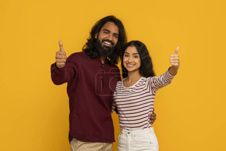 Photo for The couple cheerfully endorses with thumbs up and radiant smiles, suggesting positivity and joy on a yellow setting - Royalty Free Image