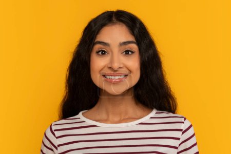Photo for A young woman in a striped shirt smiles confidently against a bright yellow backdrop, radiating positivity - Royalty Free Image