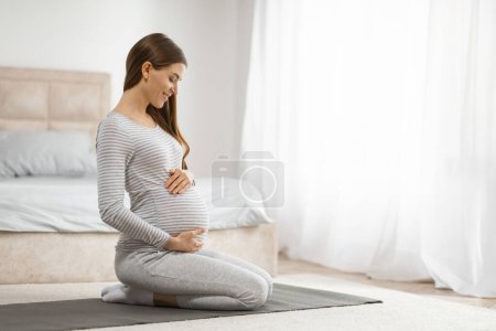 Una mujer embarazada tranquila en un estado pacífico practicando yoga prenatal en su dormitorio