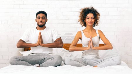 Foto de Pareja afroamericana pacífica en coordinación mientras se dedican a la meditación en su cama en casa - Imagen libre de derechos