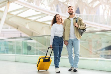 Téléchargez les photos : Un couple joyeux avec une valise jaune vif marchant et souriant à un terminal de voyage - en image libre de droit
