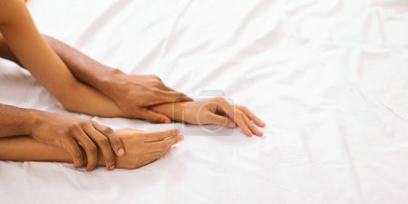 Téléchargez les photos : Les mains des couples afro-américains expriment leur proximité au lit, en mettant l'accent sur le lien qu'ils partagent au-dessus des draps blancs - en image libre de droit