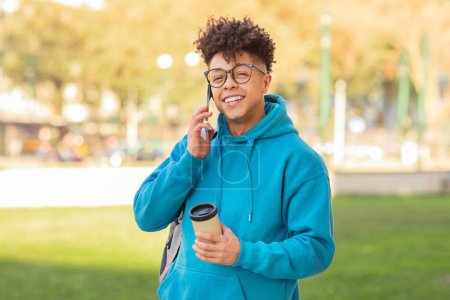 Photo for Delighted young brazilian guy multitasks by sipping coffee and engaging in a phone conversation - Royalty Free Image