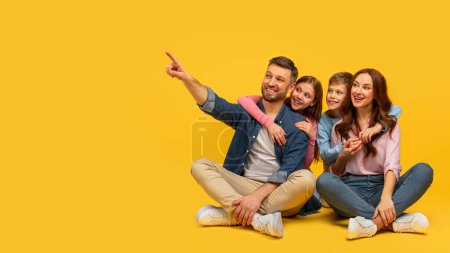A joyful family of four sitting closely, the father points away while everyone looks cheerful against a yellow background