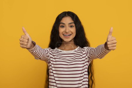 Photo for An enthusiastic woman giving two thumbs up, her bright expression matching the sunny yellow backdrop - Royalty Free Image