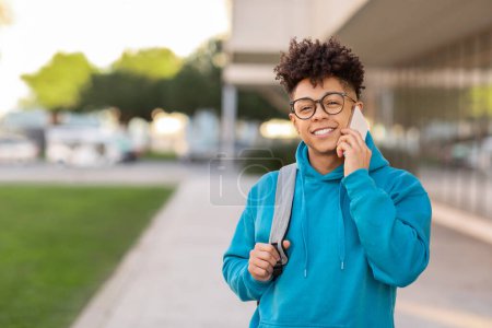 Photo for Engaged student brazilian guy with a backpack converses on the phone, with a city walking area in the background - Royalty Free Image