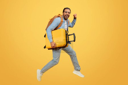 Téléchargez les photos : Homme indien énergique bondissant avec une valise, exprimant joie et excitation pour le voyage - en image libre de droit