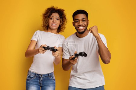 Verspieltes afroamerikanisches Paar genießt Videospiele, bei denen der Mann gewinnt und die Frau verliert und zeigt gemischte Gefühle