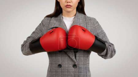 Photo for Resolute young female in business suit wearing boxing gloves, symbolizing empowerment and challenge in the corporate world, on neutral background - Royalty Free Image