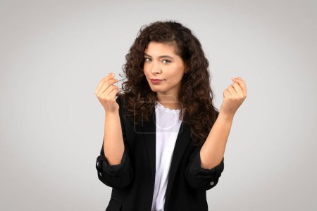 Téléchargez les photos : Une jeune femme confiante aux cheveux bouclés claque des doigts dans un studio, portant un blazer noir sur une chemise blanche - en image libre de droit
