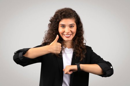 Professional woman smiling while looking at a smartwatch, possibly keeping track of schedule