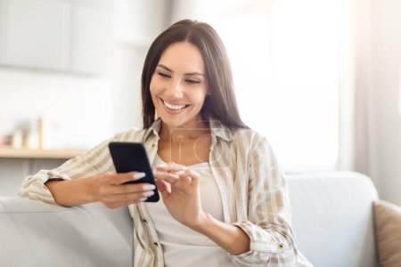 Foto de Mujer sentada cómodamente muestra una sonrisa alegre mientras escribe en su teléfono inteligente, capturando un momento de felicidad - Imagen libre de derechos